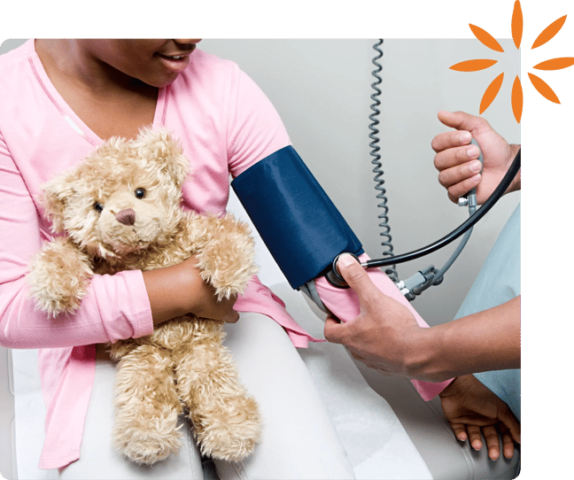 Healthcare provider checking a child's blood pressure while the child hugs a teddy bear.